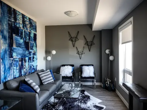 Canapé gris foncé, murs gris anthracite. Une grande toile abstraite bleue et blanche domine le salon moderne.