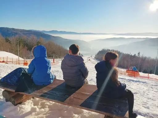 Dzieci siedzą na ławce, podziwiając widok na góra żar i dolinę spowitą mgłą.