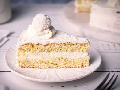 Ein saftiges Stück Raffaello Torte mit Kokosraspeln und Sahne, gekrönt von einer Raffaello-Kugel.