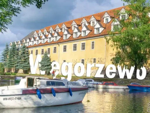 Węgorzewo atrakcje: malowniczy widok na port z łodziami i zabytkową kamienicą. Idealne miejsce na wypoczynek nad jeziorem.