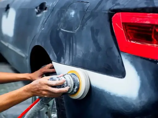 Mechanik szlifuje błotnik samochodu. Pytanie, czy benzyna ekstrakcyjna niszczy lakier, jest ważne przy takich pracach.