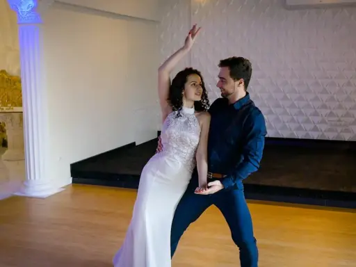 Para tańczy w białej sukni i granatowym garniturze. Ich ruchy są płynne, jakby tworzyli idealny, taneczny duet.