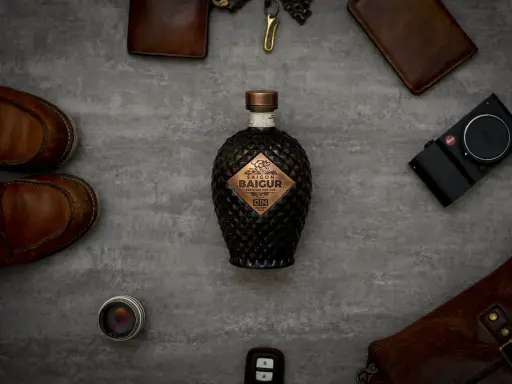 Saigon Baigur Gin mit 43% Alkoholgehalt, umgeben von Lederaccessoires, Kamera und Schuhen.