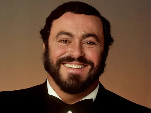 Uśmiechnięty Luciano Pavarotti w czarnym smokingu. Jego głos porusza serca, a jego uśmiech mówi "ti amo".