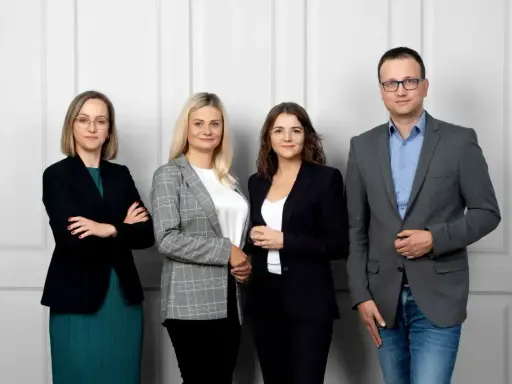 Cztery osoby w strojach biznesowych stoją obok siebie na jasnym tle.