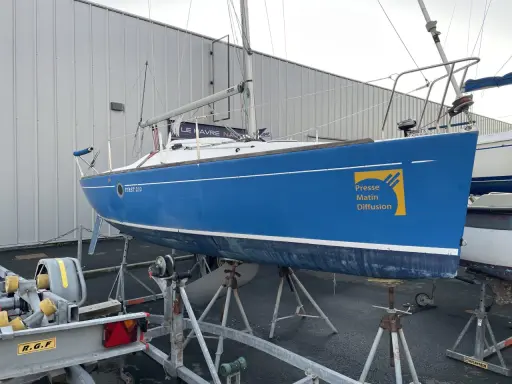 Voilier bleu FIRST 210 sur bers, prêt pour la saison. Le logo "Presse Matin Diffusion" est visible sur la coque.