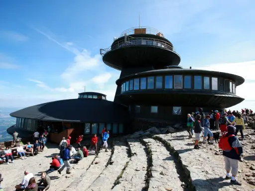 Ludzie odpoczywają na kamienistym szlaku na Śnieżkę, podziwiając widok na budynek obserwatorium.