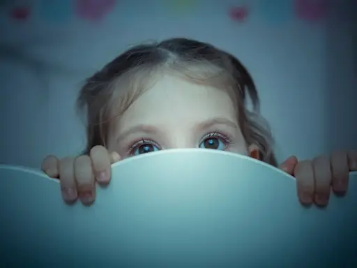 Occhi spalancati nel buio, un bambino si nasconde dietro il bordo del lettino, vittima di un pavor notturno.