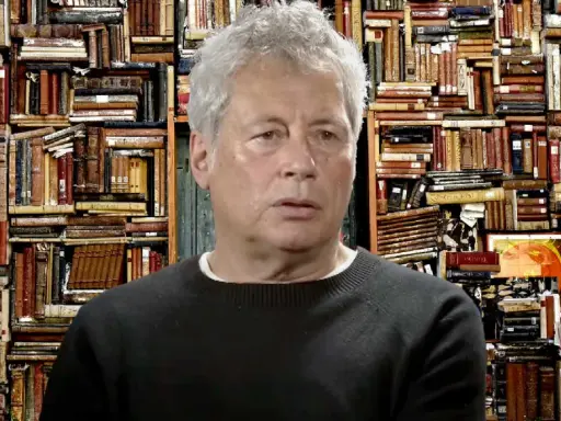 Un uomo con capelli grigi davanti a uno sfondo di libri antichi, forse ispirato ai libri di Alessandro Baricco.
