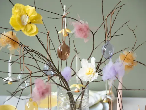 Vacker påskris inspiration med grenar dekorerade med glaskulor, tygblommor och fluffiga dekorationer i pastellfärger.