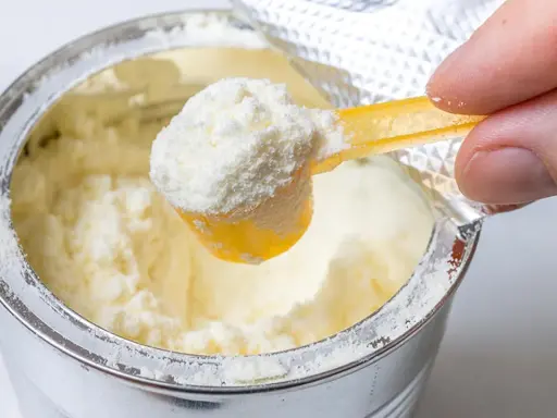 Eine Hand schöpft mit einem gelben Löffel feines Pulver aus einer Dose. Manche denken, dass Proteinpulver dick machen kann, doch es kommt auf die Menge an.