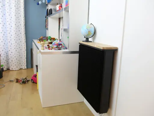 Un radiateur Qarnot particulier noir, surmonté d'un plateau en bois et d'un globe, réchauffe la chambre d'enfant remplie de jouets.
