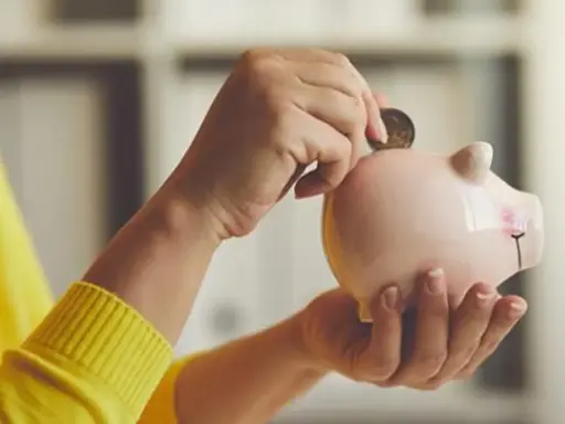 Manos introducen una moneda en una hucha rosa, simbolizando el ahorro para recuperar plan de pensiones nueva ley.