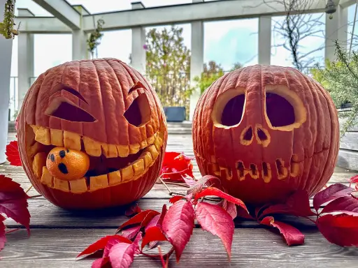 Due zucche intagliate per Halloween, una con una piccola arancia che fa la faccia spaventata. Un perfetto esempio di zucca halloween fai da te.