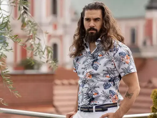 Mężczyzna z długimi włosami w hawajskiej koszuli na t-shirt, z motywem liści i ptaków.