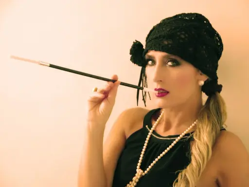 Glamurosa mujer con maquillaje de los años 20, sombrero negro y boquilla.
