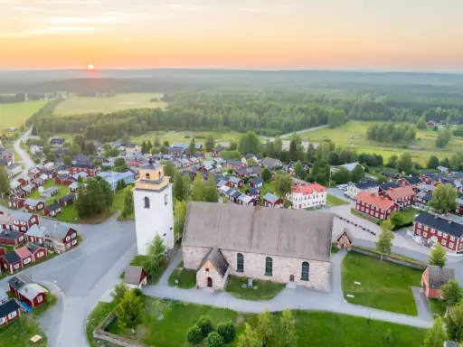 Gammelstad Luleå: en kyrka och ett kluster av röda trähus under en solnedgång.