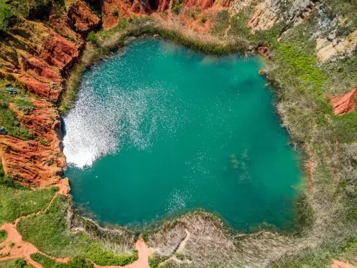 Lago turchese circondato da rocce rosse e vegetazione rigogliosa, un paesaggio suggestivo che ricorda le cave di bauxite.