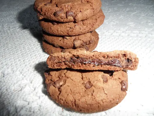 Gros plan sur une pile de biscuits au chocolat, dont un est coupé en deux révélant un cœur coulant de Nutella. Une recette de biscuit Nutella parfaite pour les gourmands.