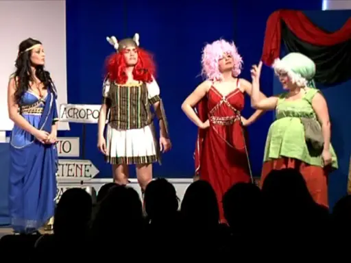 Attrici in costume su un palco, forse per la lisistrata trama. Una in blu, una guerriera, una con capelli rosa e una in verde.