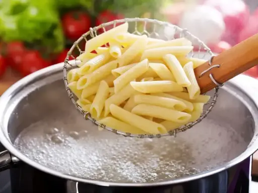 Gotowanie penne do pysznych dań z makaronem. W tle pomidory i sałata.