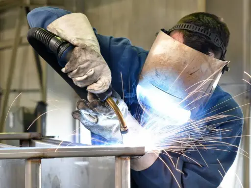 Soldador con máscara y guantes, demostrando cómo soldar con electrodo, creando chispas brillantes.
