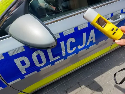Policjantka trzyma alkomat przy radiowozie. Wynik 13.7 promila to nierealny, ale symboliczny wynik dla kierowcy pod wpływem alkoholu.