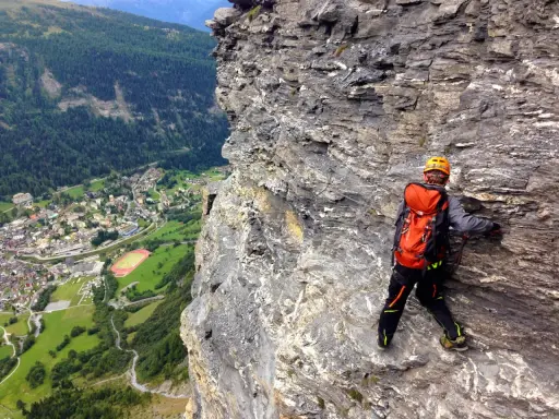Wspinaczka via ferrata w Szwajcarii. Widok na dolinę i miasteczko z perspektywy skalnej ściany.