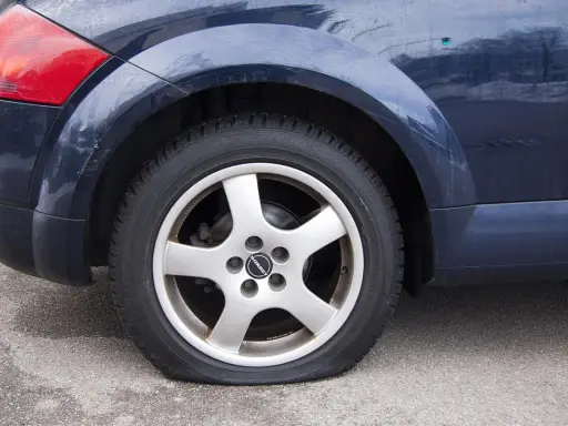 Ruota posteriore di un'auto blu con evidente perdita pressione pneumatici. Il pneumatico è sgonfio e appoggiato a terra.