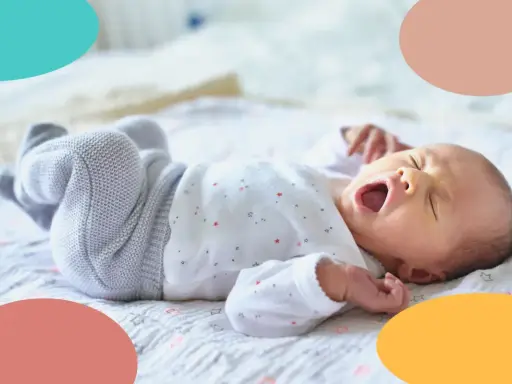 Un bebé de 1 mes bosteza, sus ojos cerrados y su boca abierta. Está acostado sobre una manta con estrellas, con las piernas cruzadas.
