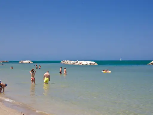 Persone si godono una giornata di sole sulla spiaggia libera di Torre Pedrera, tra bagni e relax in mare.