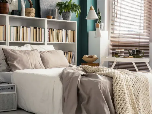 Una cama acogedora con una estantería encima llena de libros y plantas.