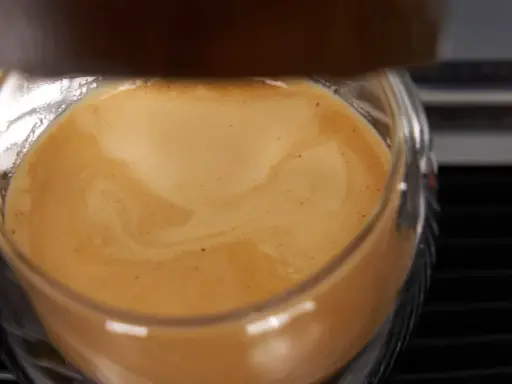 Ein Glas mit cremigem Kaffee, das ist cafe crema mit milch. Die goldbraune Crema wirbelt sanft.