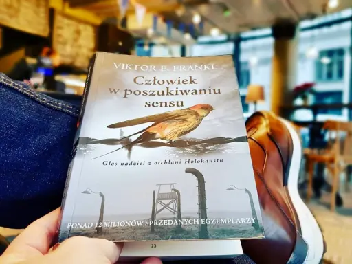 Osoba czyta "Człowiek w poszukiwaniu sensu" Viktora Frankla, szukając nadziei i znaczenia w trudnych czasach.