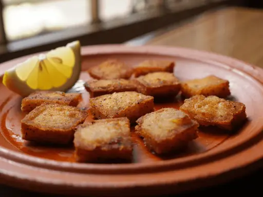Deliciosos trozos de bacalao rebozado, dorados y crujientes, servidos en un plato de barro con una rodaja de limón.