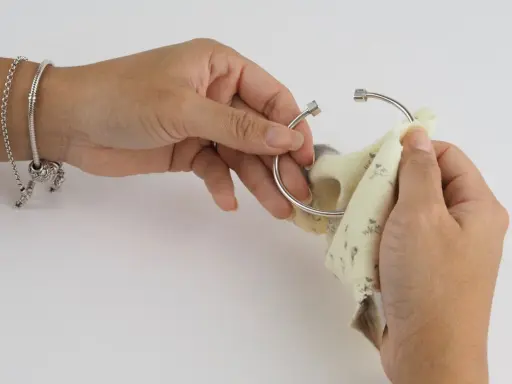 Manos puliendo un brazalete de plata con un paño. Aprende como limpiar cadena de plata y mantener tus joyas brillantes.