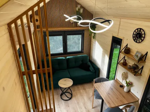 Przytulne wnętrze tiny house Polska: zielona kanapa, drewniane meble i nowoczesne oświetlenie. Idealne miejsce na relaks.