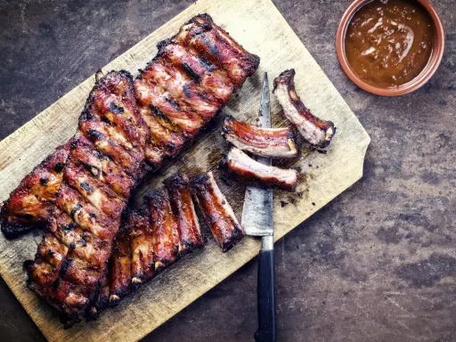 Soczyste żeberka w miodzie, grillowane do perfekcji, leżą na desce obok sosu.