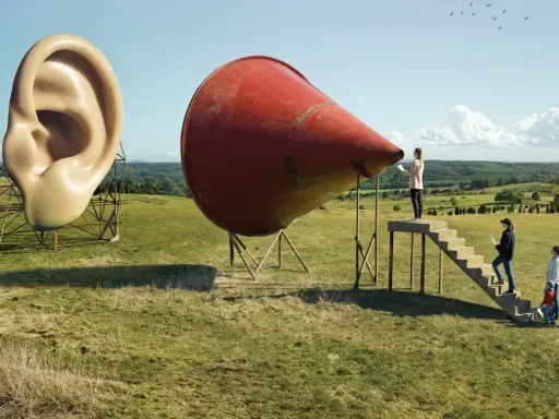 A surreal landscape by Erik Johansson photography. A giant ear stands next to a red megaphone, with people climbing stairs towards it.