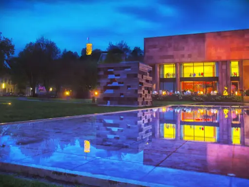 Abendstimmung am Museum mit reflektierendem Wasserbecken. Ein Turm leuchtet in der Ferne. Entdecke Bielefeld Geheimtipps!