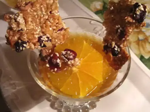 Délicieuse tuile de riz croustillante garnie de fruits secs, posée sur une tranche d'orange dans un verre.