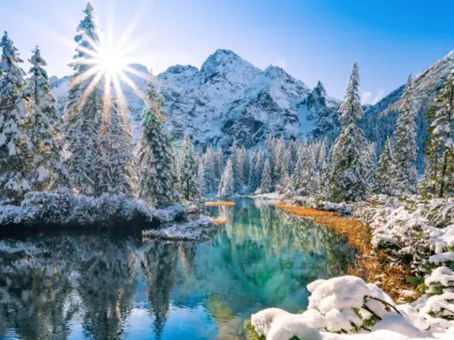 Morskie Oko zimą. Słońce przebija się przez ośnieżone drzewa, odbijając się w turkusowej tafli wody. W tle majestatyczne, pokryte śniegiem góry.