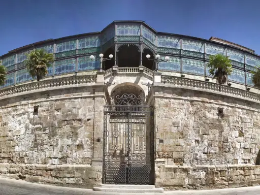 Edificio modernista en Salamanca con niños, palmeras y un cielo azul.