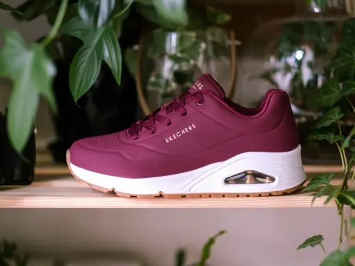 Bordowy but Skechers z białym spodem i brązową podeszwą, otoczony zielonymi liśćmi. Dowiedz się, jak wyczyścić sznurówki, aby buty wyglądały jak nowe.