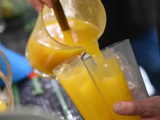 Ein Mann gießt leuchtend gelben Saft, vielleicht Poncha Madeira, aus einer Glaskaraffe in zwei Gläser mit Eiswürfeln.
