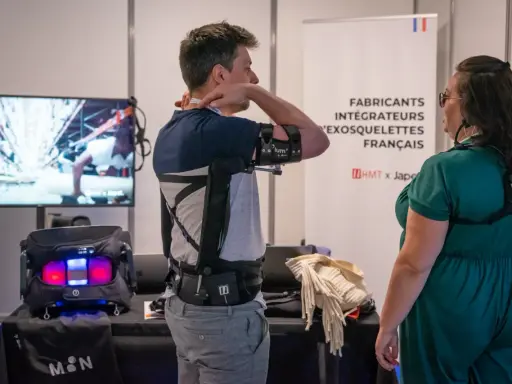 Un homme teste un exosquelette pour le bras, une technologie d'assistance pour le handicap. Une femme observe.