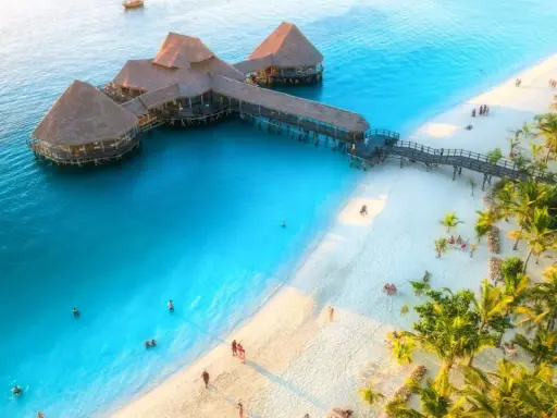 Zanzibar w czerwcu: idealna pogoda na wypoczynek na rajskiej plaży z turkusową wodą i palmami. Widać hotel na wodzie i ludzi kąpiących się.