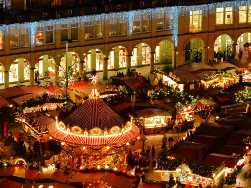 Vista aérea de mercadillos navideños iluminados, con un carrusel festivo y puestos de comida.