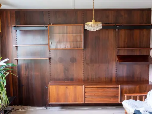 En väggmonterad hylla i teak, troligen designad av Poul Cadovius, med glasmonter, lådor och hyllplan.