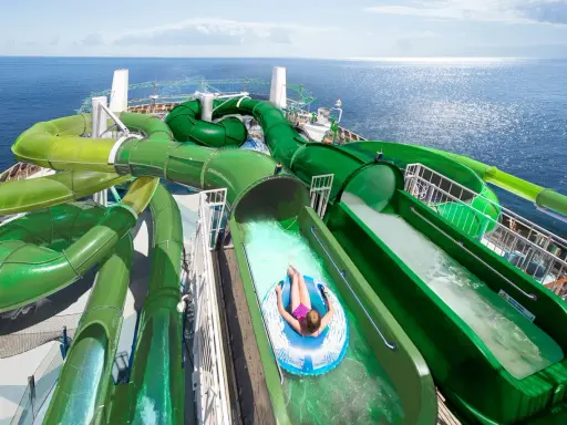Divertente crociera per bambini con scivoli acquatici verdi che si snodano sul ponte di una nave da crociera, con il mare blu sullo sfondo.